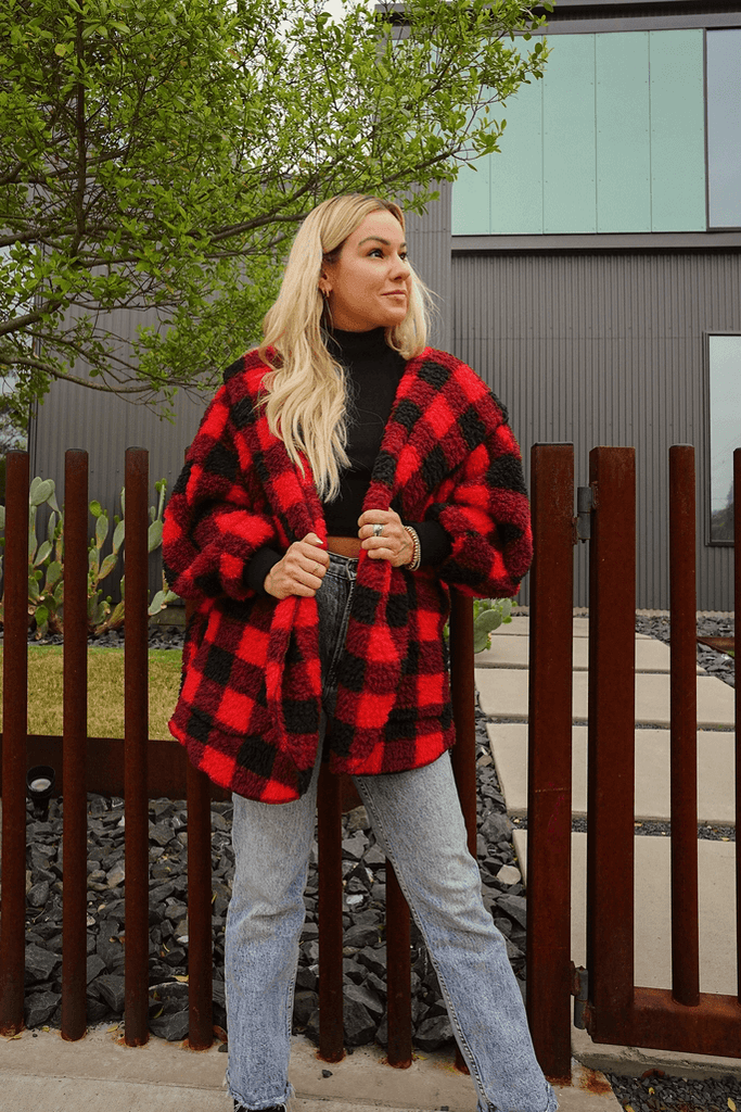 woman wearing jeans and plaid wrap cardigan standing outside by a fence