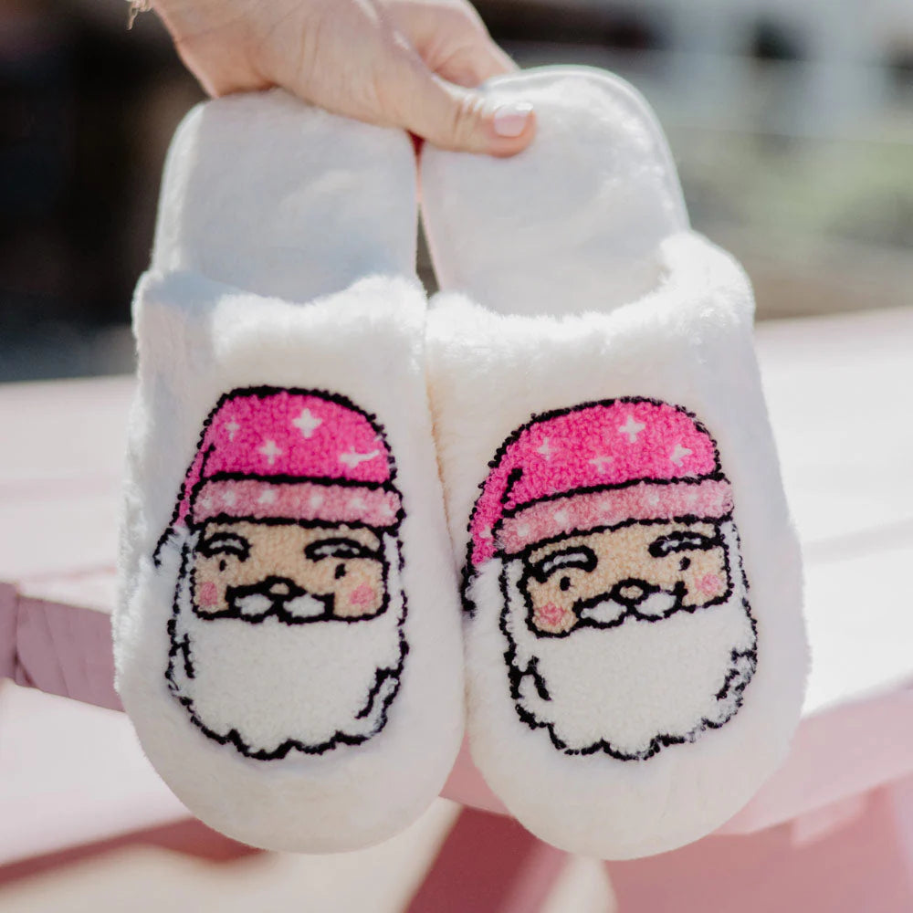 Person holding up a pair of white fluffy Christmas slippers with Santa faces