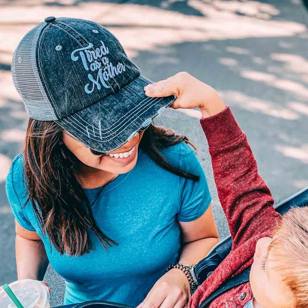  A kid putting a “Tired as a mother” trucker hat on mom