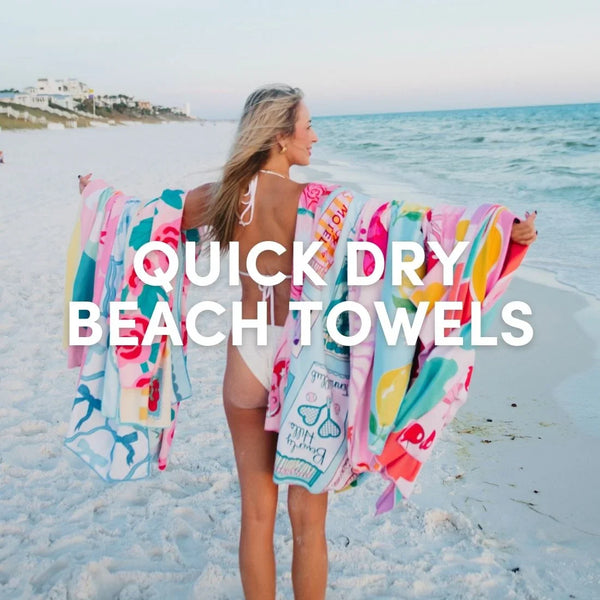 Woman walking along the beach at sunset wearing a white swimsuit and holding colorful Katydid quick dry beach towels draped over her arms.