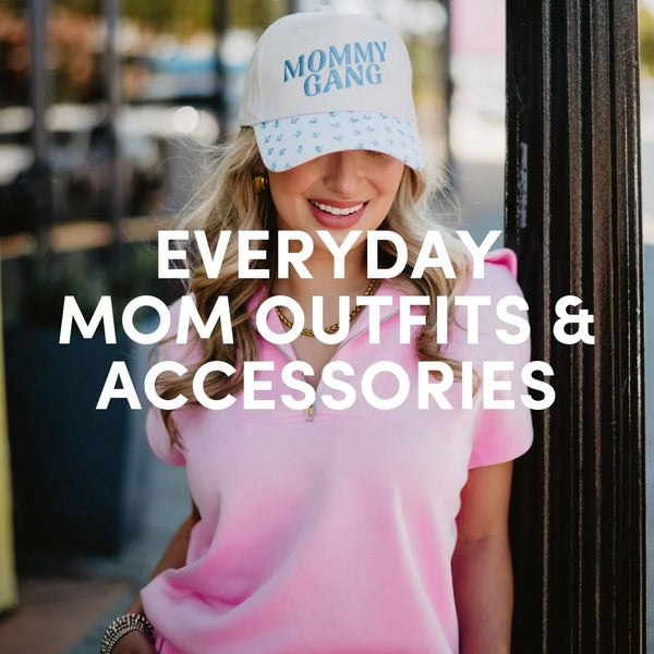 Woman wearing a pink top and a “Mommy Gang” embroidered trucker hat styled with gold jewelry, representing everyday mom outfits and accessories.