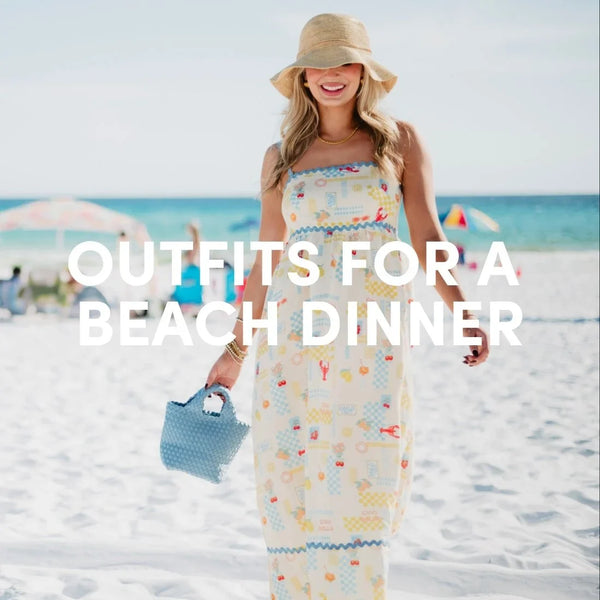 Woman wearing a patterned maxi dress and straw sun hat walking on the beach holding a woven handbag, with “Outfits for a Beach Dinner” text overlay