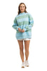 A woman smiles, wearing the Katydid Aqua and Green Striped Mockneck Sweatshirt for women, styled oversize with a white shirt underneath and white sneakers. She stands against a plain white background.