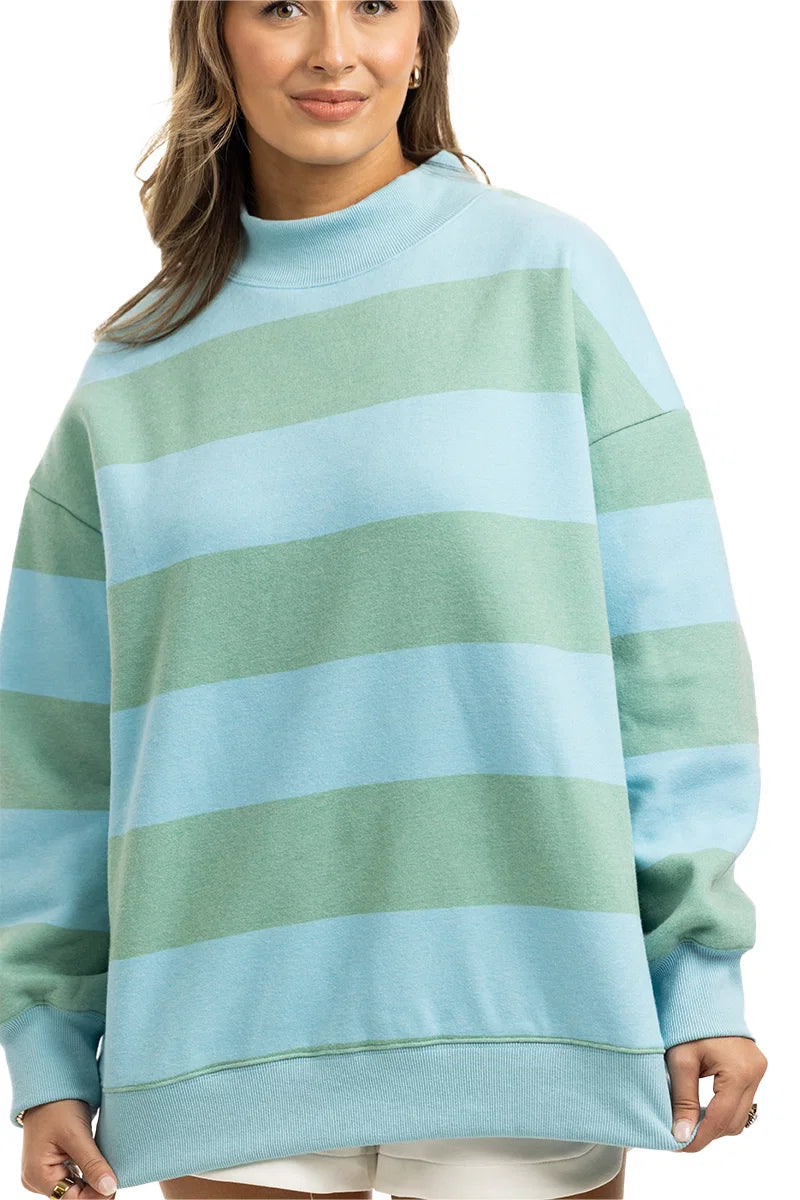 A woman models the Katydid Aqua and Green Striped Mockneck Sweatshirt, featuring oversized horizontal stripes, against a white background.