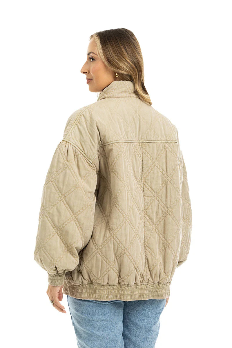 A woman stands with her back to the camera, wearing the Katydid Beige Luxe Oversized Jacket with puffy sleeves and blue jeans, set against a white background.
