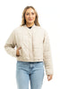 A woman wearing the Katydid Beige Quilted Bomber Fall Jacket with snap buttons and blue jeans stands against a white background, smiling.