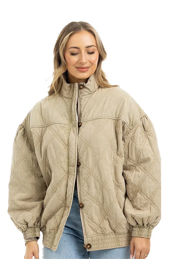 A woman with light brown hair smiles gently while wearing the Katydid Beige Luxe Oversized Jacket and blue jeans against a plain white background.