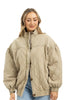 A woman with light brown hair smiles gently while wearing the Katydid Beige Luxe Oversized Jacket and blue jeans against a plain white background.