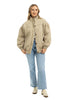 A woman smiles in the Katydid Beige Luxe Oversized Jacket, styled with light blue jeans and beige sneakers. Her blonde hair frames her face as she poses against a white background, highlighting the jacket’s comfort and style.