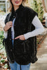 A woman in a white long-sleeve shirt, blue jeans, and a Katydid Charcoal Oversized Garment Washed Quilted Vest with front pockets stands on a path, holding the vest open with one hand and smiling slightly.