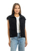 A woman with long brown hair parted in the middle faces forward, modeling the Katydid Black Corduroy Trendy Puffer Vest over a white tee and light blue jeans against a neutral background.