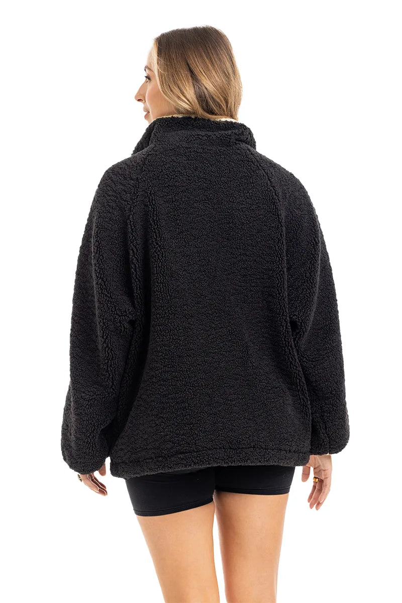 A woman with light brown hair is seen from the back wearing the Katydid Black Sherpa Lace Trim Jacket and black shorts, posed against a white background.