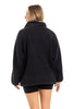 A woman with light brown hair is seen from the back wearing the Katydid Black Sherpa Lace Trim Jacket and black shorts, posed against a white background.