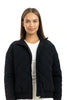 A woman with straight brown hair wears a white shirt and the Katydid Black Sporty Diamond Quilted Jacket, standing against a plain white background and smiling gently at the camera—ideal as a stylish fall jacket.