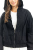 A woman models the Katydid Black Lightweight Hooded Cute Jacket over a white top, hood up and brown hair showing, against a white background.