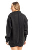 A person with light brown hair faces away, wearing the Katydid Black Vintage Wash Pullover Sweatshirt, which has visible seams down the back and shoulders, paired with black shorts. The background is plain white.