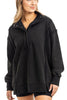 A woman wears the Katydid Black Vintage Wash Pullover Sweatshirt, featuring a loose fit, partial button-up collar, and long sleeves, standing with one hand relaxed by her side.