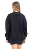 A woman with light brown hair is standing and facing away from the camera against a white background, wearing a Katydid Black Mockneck Sweatshirt and black shorts.