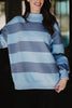 A woman wears the Katydid Light Blue and Navy Striped Mockneck Sweatshirt, smiling with one arm raised. This cozy layering piece stands out against a dark, blurred background.