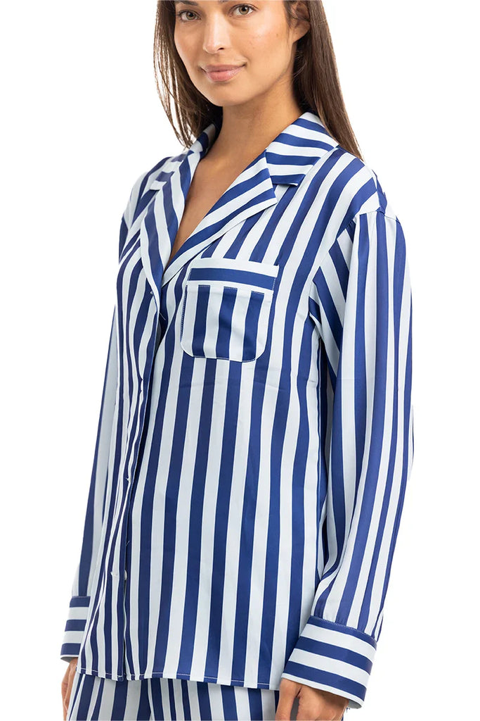A woman stands and smiles slightly, wearing the Katydid Light Blue and Navy Striped Satin Pajama Matching Set with long sleeves and a chest pocket.