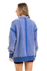 A woman with long, light brown hair is shown from the back wearing the Katydid Blue Vintage Wash Snap-Neck Pullover with visible seam details, paired with black shorts against a plain white background.