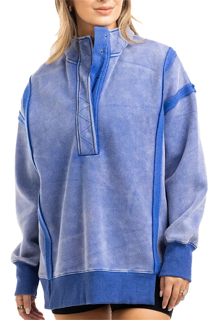 A person wears the Katydid Blue Vintage Wash Snap-Neck Pullover featuring a high snap-button collar, exposed seam details, and an oversized fit, paired with black shorts.