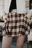 A person wears a beige jacket and a Brown Plaid Bubble Hem Skirt with hands in pockets. The skirt’s waistband features a Katydid label.