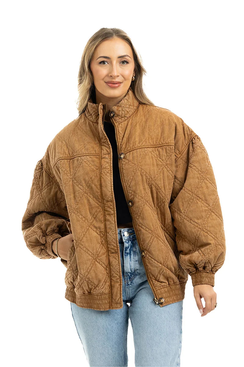 A woman smiles against a white background, wearing the Katydid Brown Luxe Garment Washed Oversized Jacket over a black top and light blue jeans.