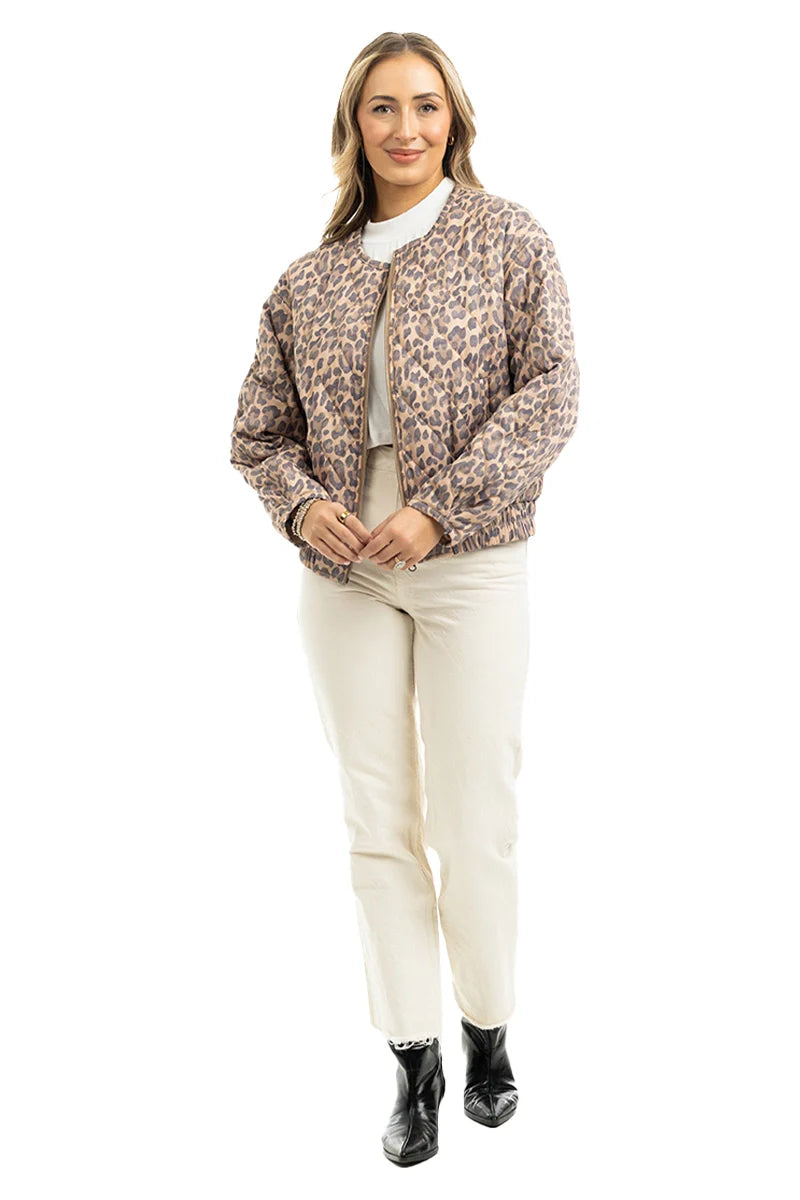 A woman faces forward, smiling in the Katydid Brown Leopard Quilted Jacket paired with a white top, light pants, and black ankle boots against a white background.