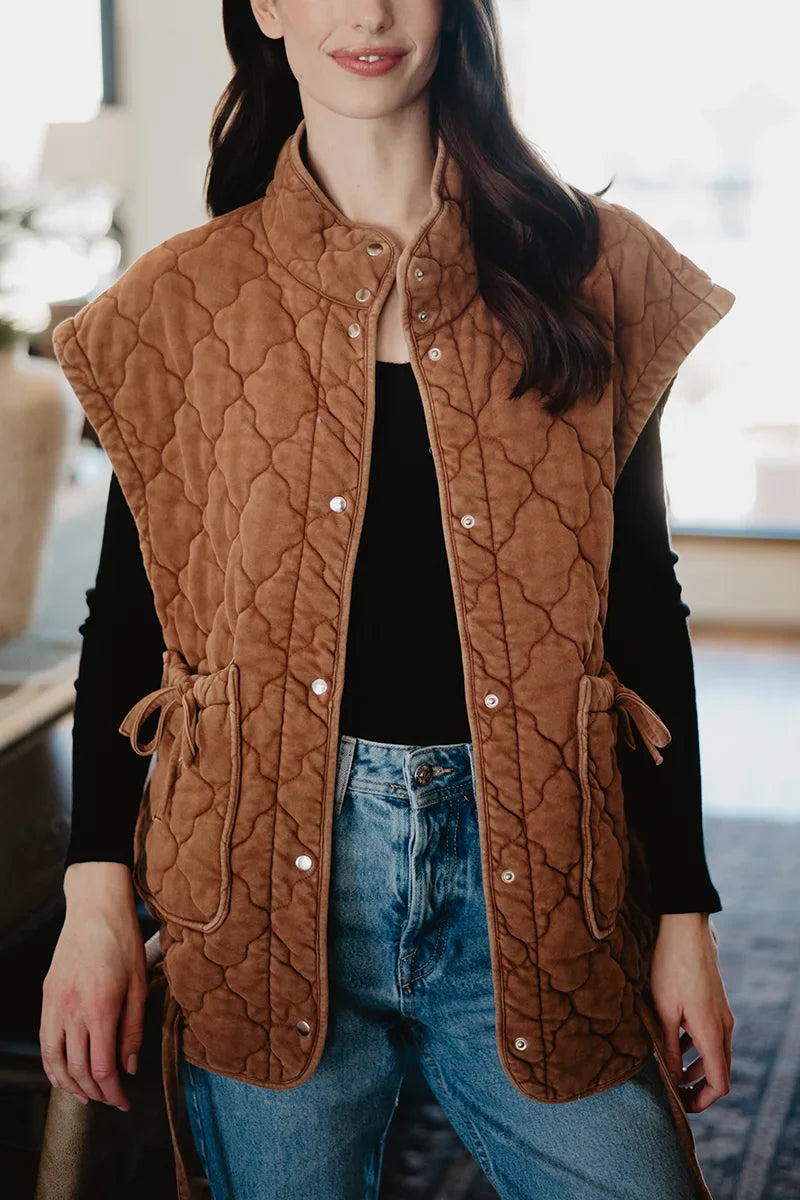 A woman models the Katydid Brown Oversized Womens Quilted Vest with short sleeves over a black top and blue jeans—a chic, stylish fall look.