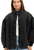 A woman wearing the Katydid Womens Charcoal Luxe Oversized Jacket stands facing the camera with a slight smile, pairing it with a white top and blue jeans.