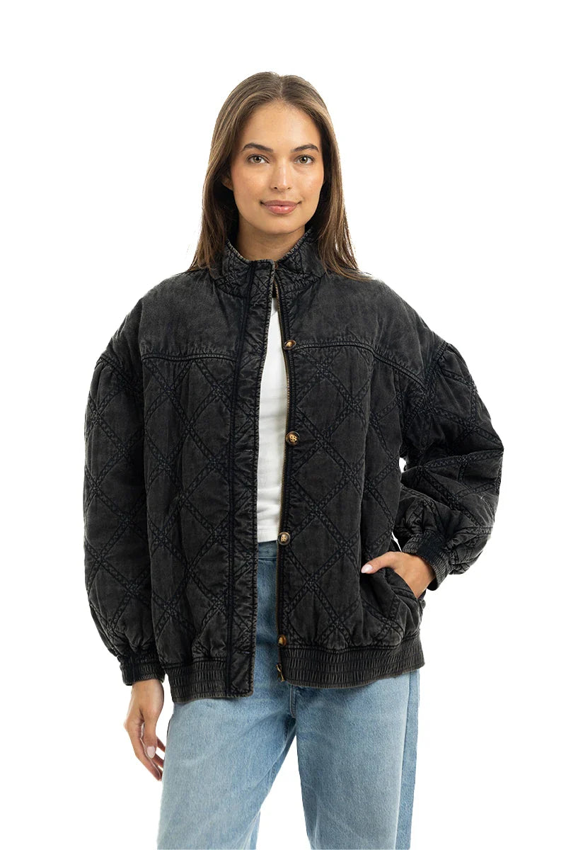 A woman stands against a white background, wearing the Katydid Womens Charcoal Luxe Oversized Jacket featuring a vintage vibe, stand-up collar, button closure, side pockets, and relaxed fit over a white top and light blue jeans.