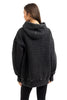 A person with long brown hair, wearing a Katydid Charcoal Heart Quilted Pullover Hoodie and black leggings, stands facing away and looks slightly to the side.