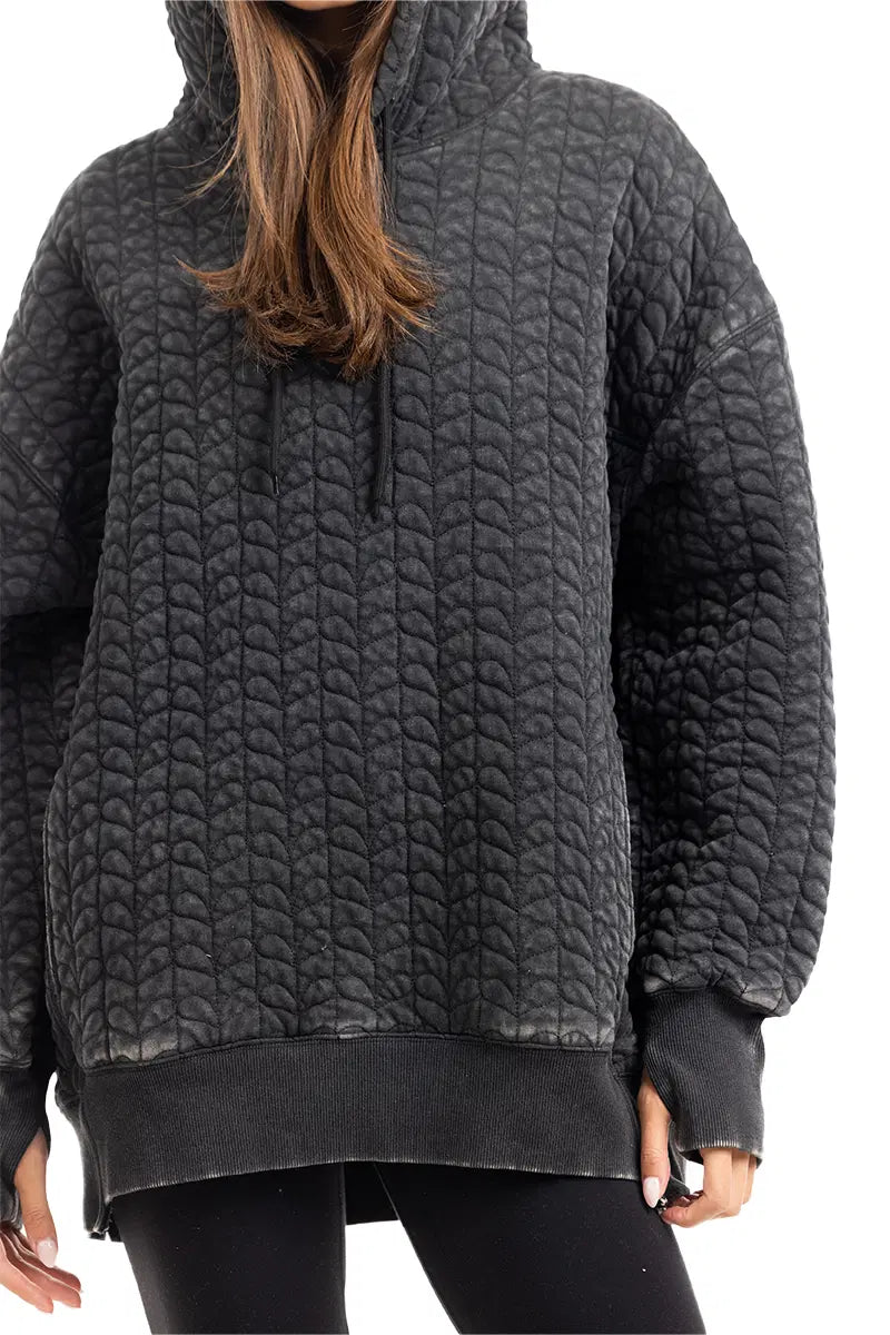 A person wears the Katydid Charcoal Heart Quilted Pullover Hoodie with a scalloped pattern and long sleeves, paired with black leggings. The hoodie is oversized and textured, and the person’s face is not visible.