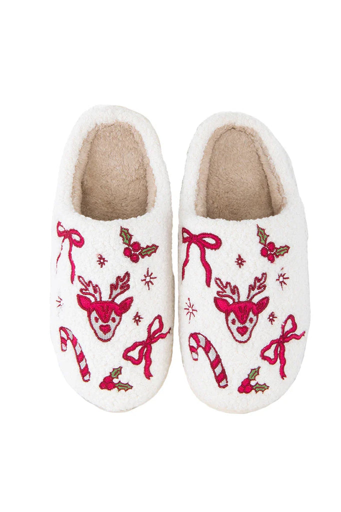 The Katydid Bow Reindeer Winter Slippers feature white fuzzy sherpa, red reindeer faces, bows, candy canes, holly leaves, and snowflakes, with a soft beige inner lining for comfort. Seen from above.