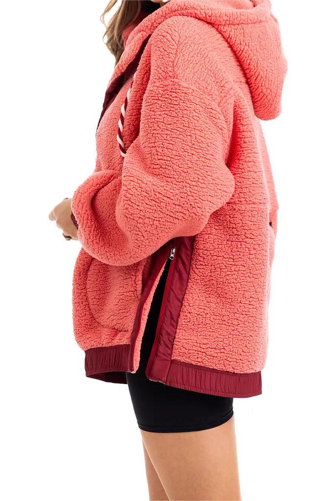 A woman models the Katydid Coral Two-Toned Womens Fleece Pullover, featuring maroon trim, paired with black shorts. She stands sideways, and only her upper body is visible.