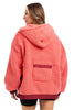 A woman with light brown hair faces away, wearing the Katydid Coral Two-Toned Womens Fleece Pullover with a hood and small back pocket, paired with black shorts.
