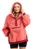 A woman smiles in the Katydid Coral Two-Toned Womens Fleece Pullover, featuring a cozy sherpa design, front zipper, white striped drawstrings, and maroon accents. She pairs it with black shorts and rests one hand on the hoodie.