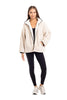 A woman poses confidently against a white background in the Katydid Cream Womens Sherpa Lace Trim Jacket, styled over a black top and leggings with light sneakers. Her long hair adds to the effortlessly stylish, cozy fall look.