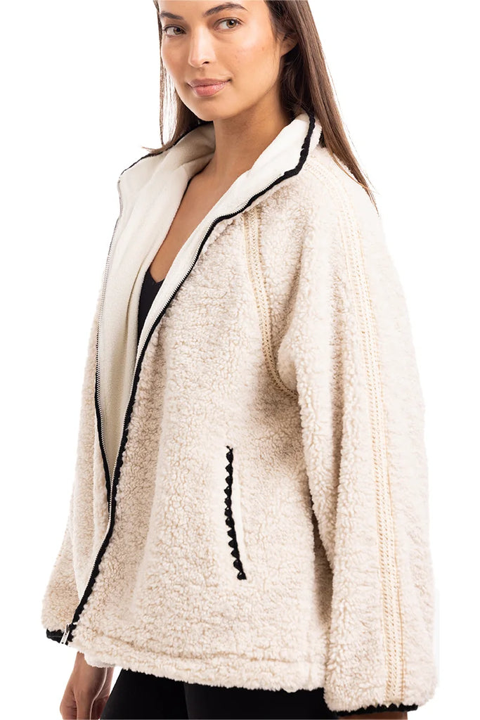 A woman wearing the Katydid Cream Womens Sherpa Lace Trim Jacket stands sideways, smiling slightly. This cozy fall jacket features a soft texture, relaxed fit, and lace trim—perfect for chilly days.