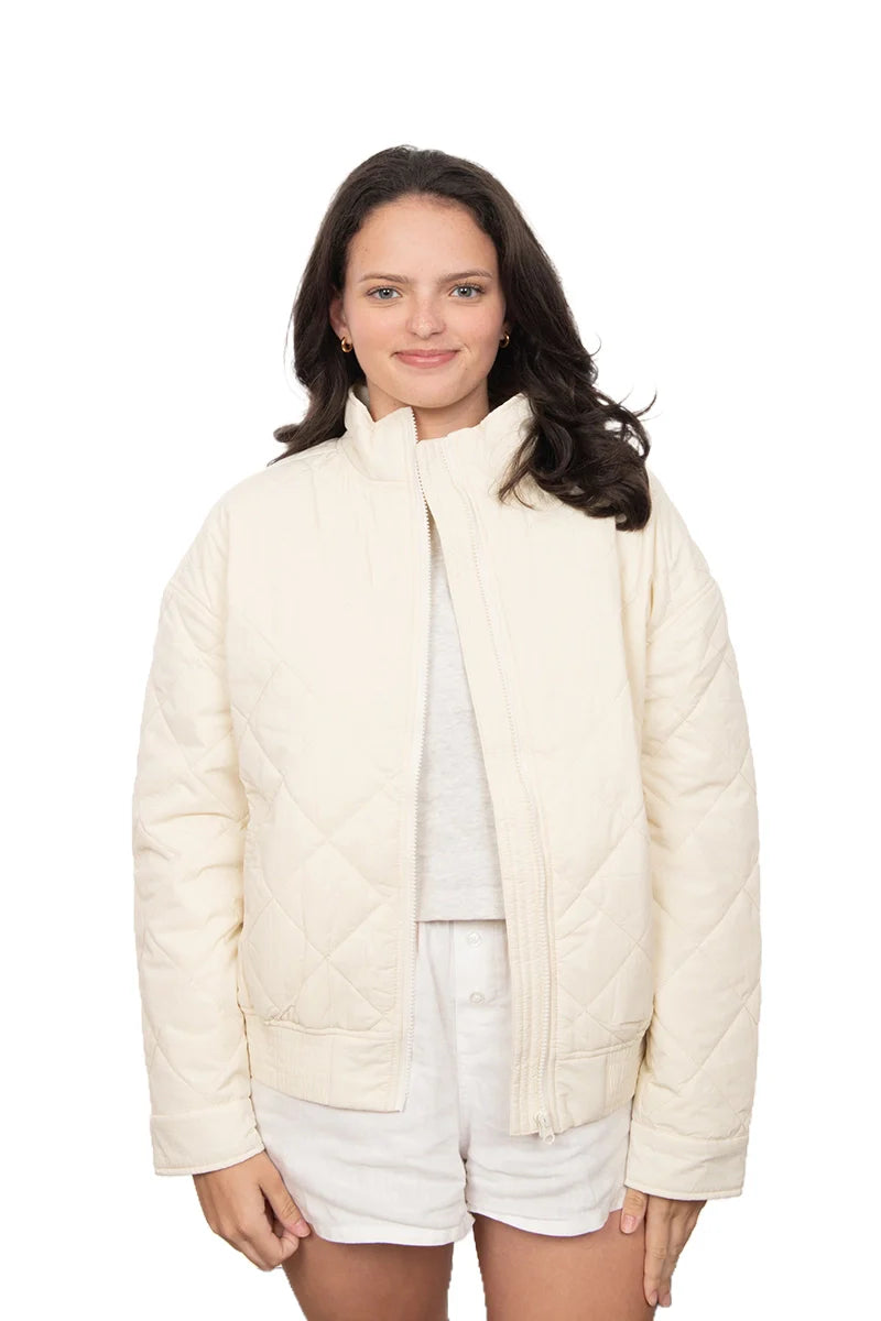 A woman with dark hair wears the Katydid Cloud White Sporty Diamond Quilted Jacket over a white shirt and white shorts, standing against a plain white background.