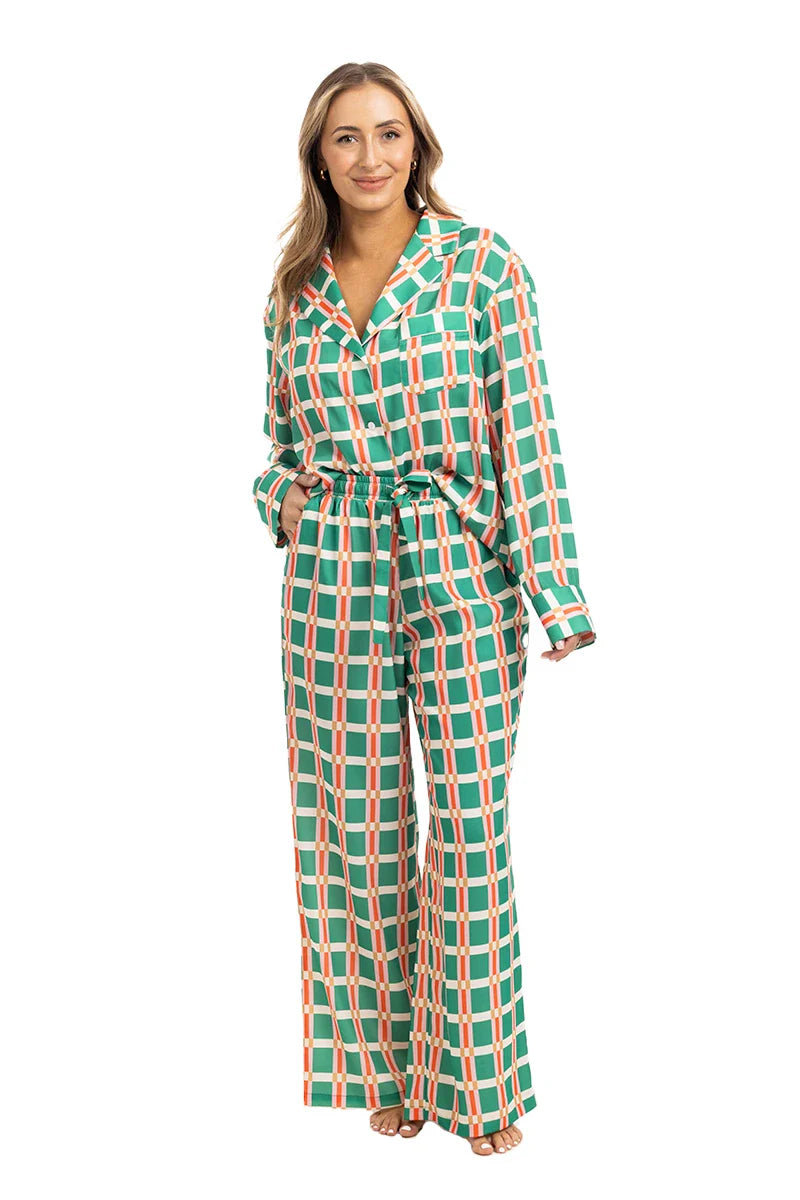 A woman wears the Katydid Green  Pink Plaid Pajama Pants Set, featuring loose, wide-leg pants and a long-sleeved top, with tan sandals against a white background.