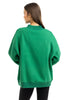 A woman with long brown hair, seen from behind, wears the Katydid Red Plaid Bow Mockneck Sweatshirt for women and black pants against a plain white background—a perfect cozy holiday look.