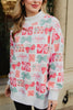 A woman stands outside, smiling in the Katydid Wrapped Presents with Bows Mockneck Pullover— a festive sweatshirt with colorful red, pink, and green gift boxes and bows, white cuffs, and a crisp white mockneck collar.