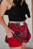 A person in a black sleeveless top and Katydid’s Royal Stewart Plaid Mini Bubble Skirt lifts the skirt to show red liner shorts underneath. The visible torso and upper legs make this a fun, festive holiday party look.