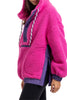A person wears the Katydid Hot Pink Two-Toned Sherpa Pullover Jacket with purple accents, white-and-purple drawstrings, large pockets, and a side zipper, paired with black leggings. Their face is partially out of frame.