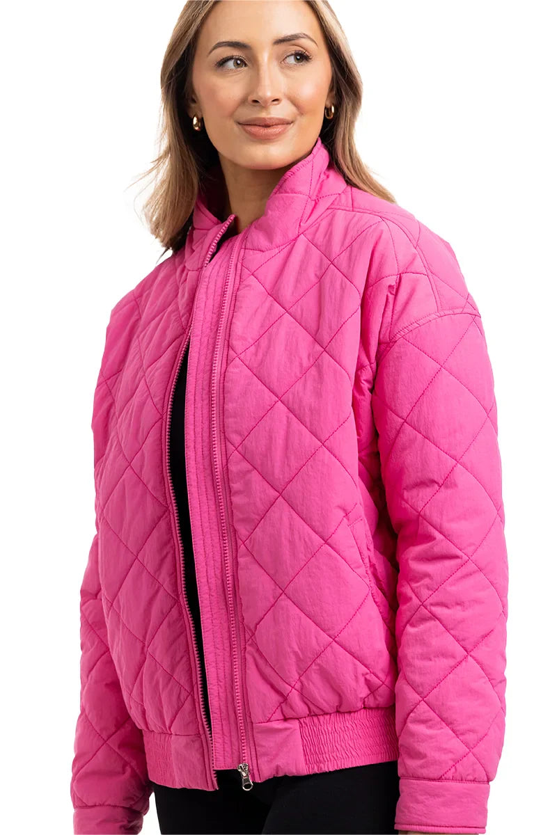 A woman with light brown hair smiles while wearing the Katydid Hot Pink Sporty Diamond Quilted Jacket, featuring a zipper front and diamond stitching. This stylish, lightweight jacket is perfect for fall and stands out against a white background.