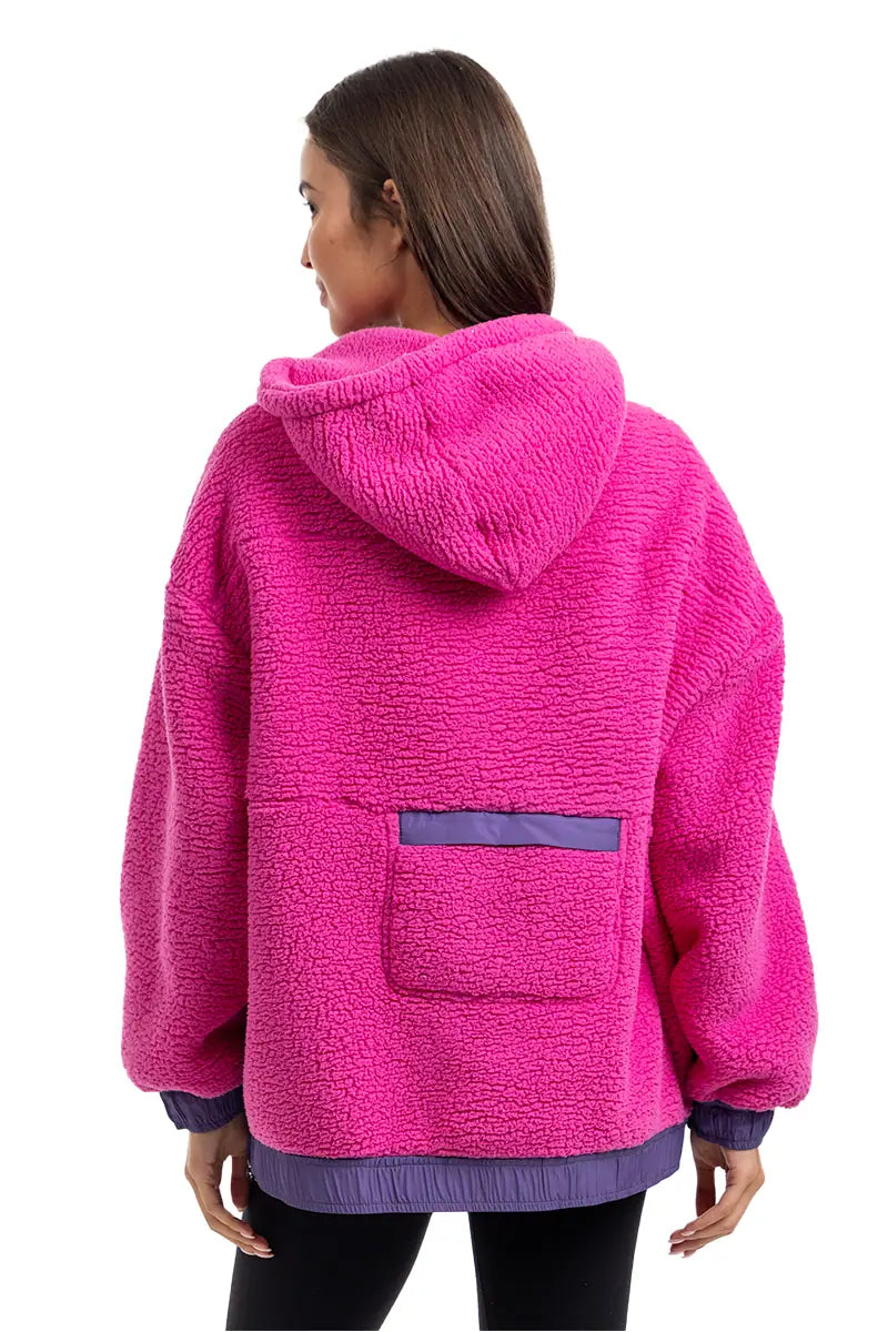 A person with long brown hair is seen from behind wearing the Katydid Hot Pink Two-Toned Sherpa Pullover Jacket, which features cozy purple trim and a purple lower back pocket.