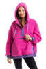 A woman smiles at the camera in the Katydid Hot Pink Two-Toned Sherpa Pullover Jacket, featuring a purple front pocket, trim, and hood, paired with black leggings.