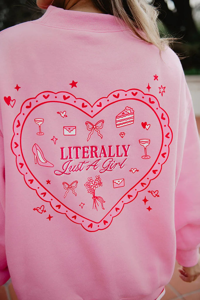 A person wears the Katydid Literally Just A Girl Mockneck Pullover, a cute pink sweatshirt with a large red heart on the back featuring embroidered shoes, bows, drinks, flowers, cake, and Literally Just A Girl in the center.